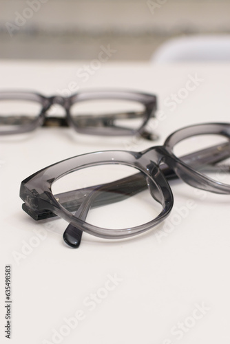 Gafas gruesas de acr  lico en tono gris sobre fondo blanco. Fotograf  a vertical de producto con desenfoque. Recurso gr  fico.