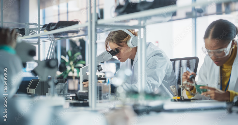 Team of Multiethnic Science Students Conducting Electronics Experiments in a University Workshop. Diverse Young Classmates Using Microscopes, Working with Soldering Iron to Create a Circuit Board