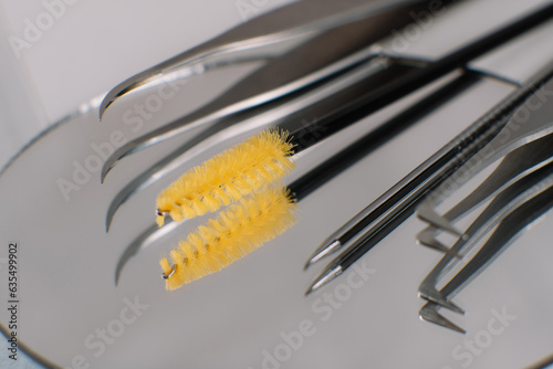 Various professional tools for eyelash extension procedure left on round mirror on table, reflecting in looking-glass.