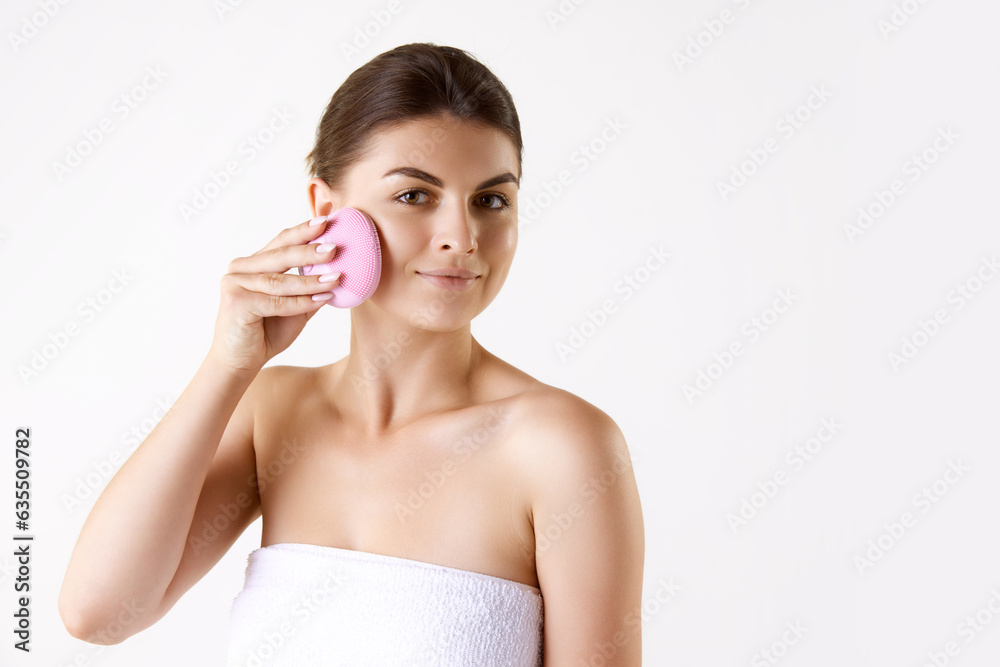 Attractive woman after shower, in towel cleansing face with special face tool against white studio background. Concept of female beauty, skin care, cosmetology and cosmetics, health, ad Attractive woman after shower, in towel cleansing face with special face tool against white studio background. Concept of female beauty, skin care, cosmetology and cosmetics, health, ad