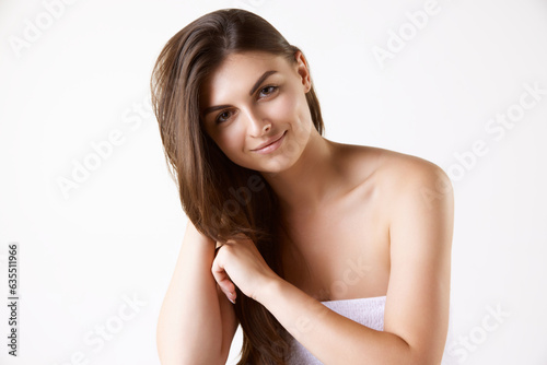 Portrait of beautiful brunette young woman with long straight hair, standing in towel against white studio background. Concept of female beauty, hair care, cosmetology and cosmetics, health, ad