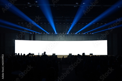 Front view of mockup on big blank white screen with space in huge hall and silhouette of audiences