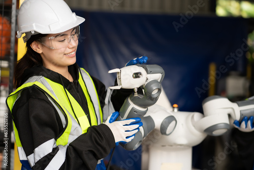 Electronic and robotic engineer working on robot arm maintenance in AI futuristic innovation technology factory. Women technician wear hardhats examining artificial intelligence automated machine.