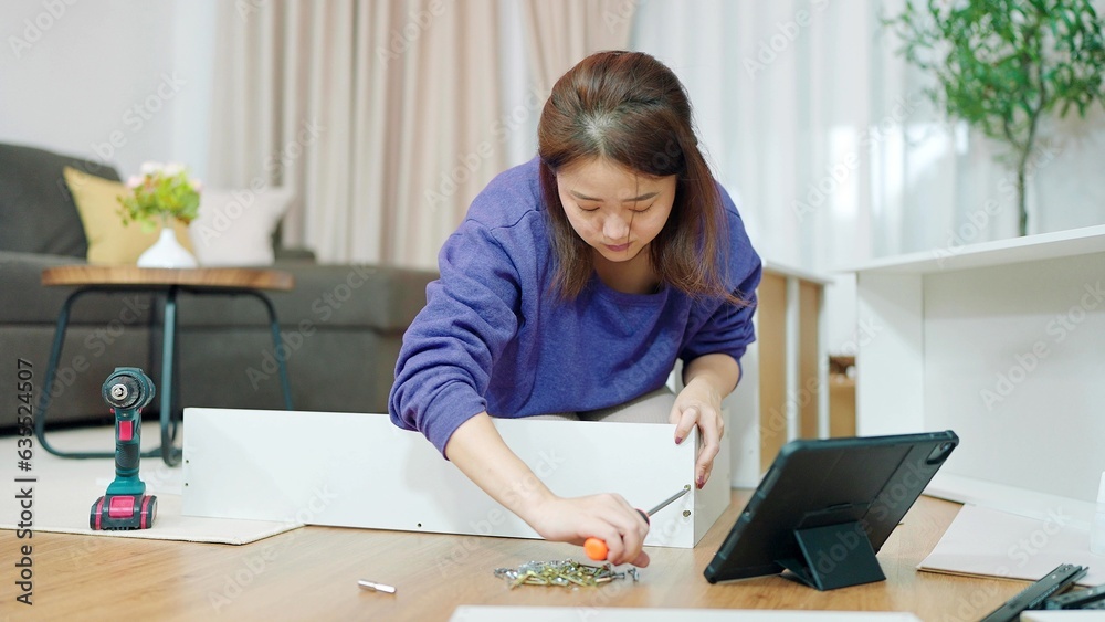 Young asian women using tightens screw for assembling new furniture by herself at home. Assembling furniture concept