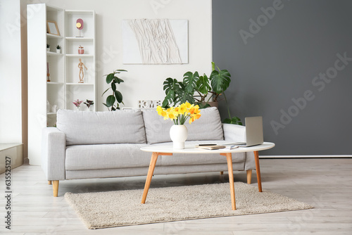 Interior of stylish living room with modern laptop and flower vase on coffee table