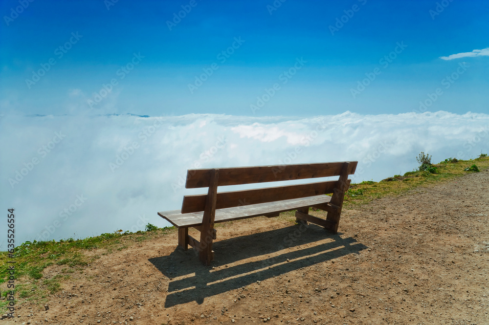 Bench without people on precipice above the clouds.