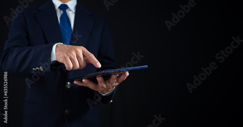 Businessman standing and holding tablet on dark background. Copy space. banner sign
