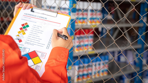 A worker is checking on the hazardous chemical material information form with background of chemical storage area at the factory place. Industrial safety working action. Selective focus. photo