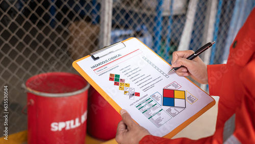 Action of safety officer is checking chemical hazard material form for correct the oil spill kit which is placed at front of chemical storage warehouse area in factory. Close-up and selective focus. photo