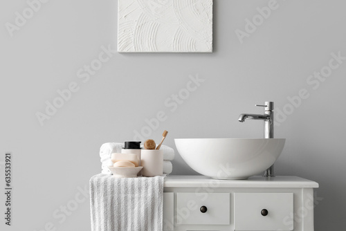 Sink bowl and bath accessories on table in light bathroom