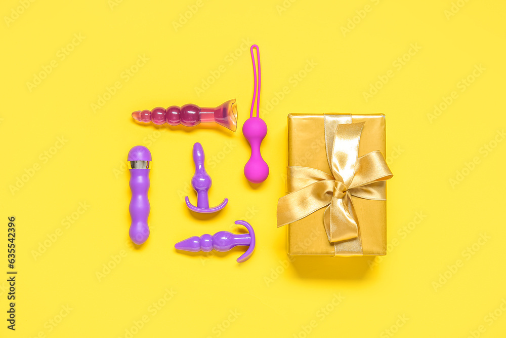 Composition with different sex toys and gift box on yellow background