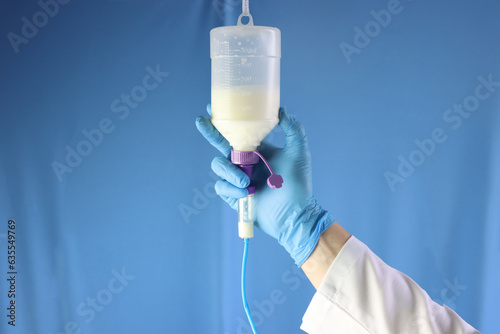 Enteral nutrition diet bottle hanging and infusing enteral diet throughout an infusion set. Professional holding and checking the diet. Blue background