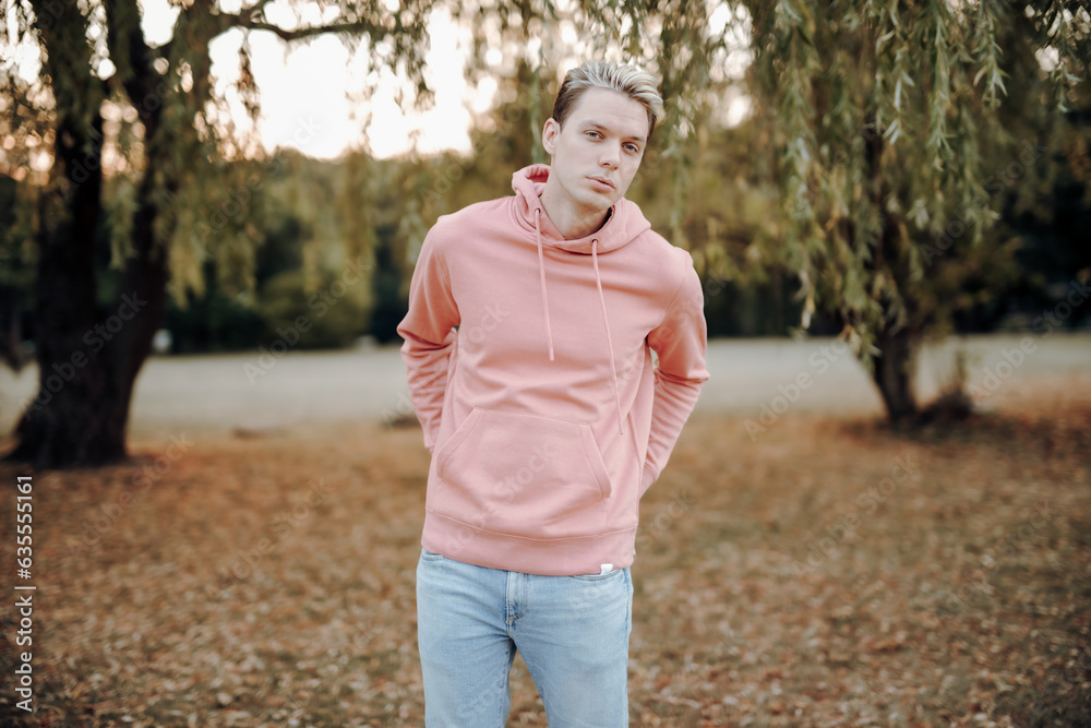 handsome guy stand outside in park, with hands behind body, wear a pink sweater, look serious at camera while he pose stylishly and confidently, embody the fashion trends of youth handsome guy stand outside in park, with hands behind body, wear a pink sweater, look serious at camera while he pose stylishly and confidently, embody the fashion trends of youth