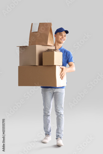Young courier with parcels on light background © Pixel-Shot
