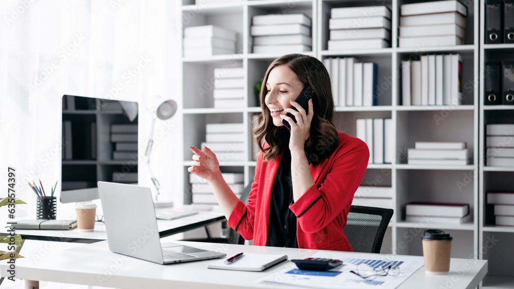 Businesswoman using smartphone talking and looking business data on laptop while working about analysis of strategy and planning new business in office Businesswoman using smartphone talking and looking business data on laptop while working about analysis of strategy and planning new business in office