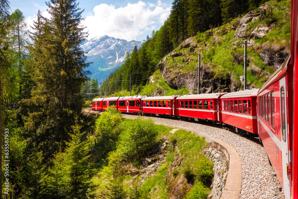 Red train moving in beautiful green summer forest in Switzerland