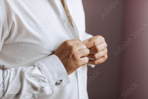 Close-up of a man buttoning his shirt. The groom is preparing for the wedding. The man wears a white shirt. Stylish groom