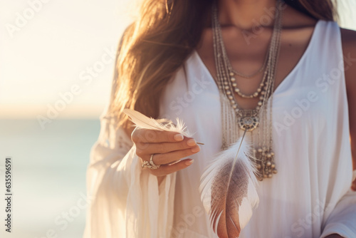 Woman with boho jewellery holding a feather in her hands close up. Spirituality, harmony and connection with nature concept.
