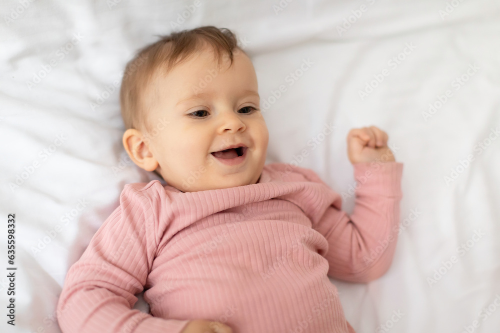 Portrait of cute little baby girl lying and smiling posing on white blanket on bed, above view shot, free space Portrait of cute little baby girl lying and smiling posing on white blanket on bed, above view shot, free space