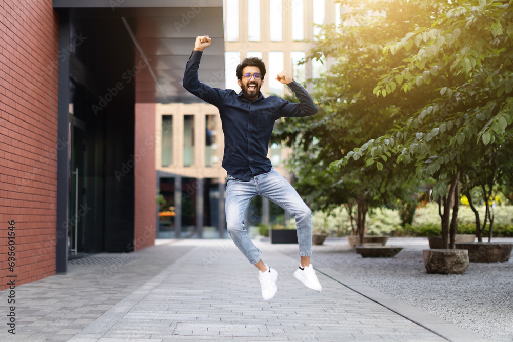 Thrilled young eastern man celebrating success, jumping on street