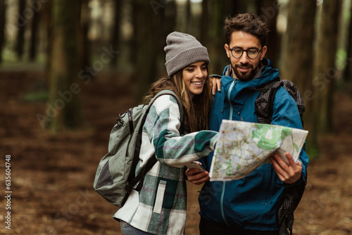 Cheerful young caucasian couple in jackets enjoy travel, vacation, look at map for route in forest #635604748