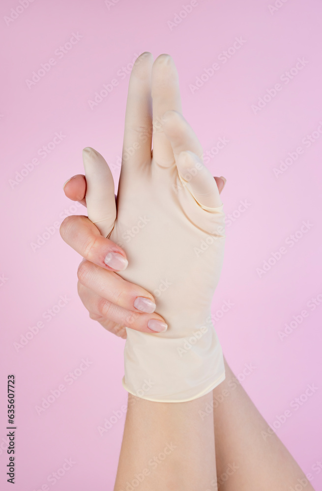 Elegant female hands, one of which is in a white latex glove on a pastel pink background. Close up. Elegant female hands, one of which is in a white latex glove on a pastel pink background. Close up.