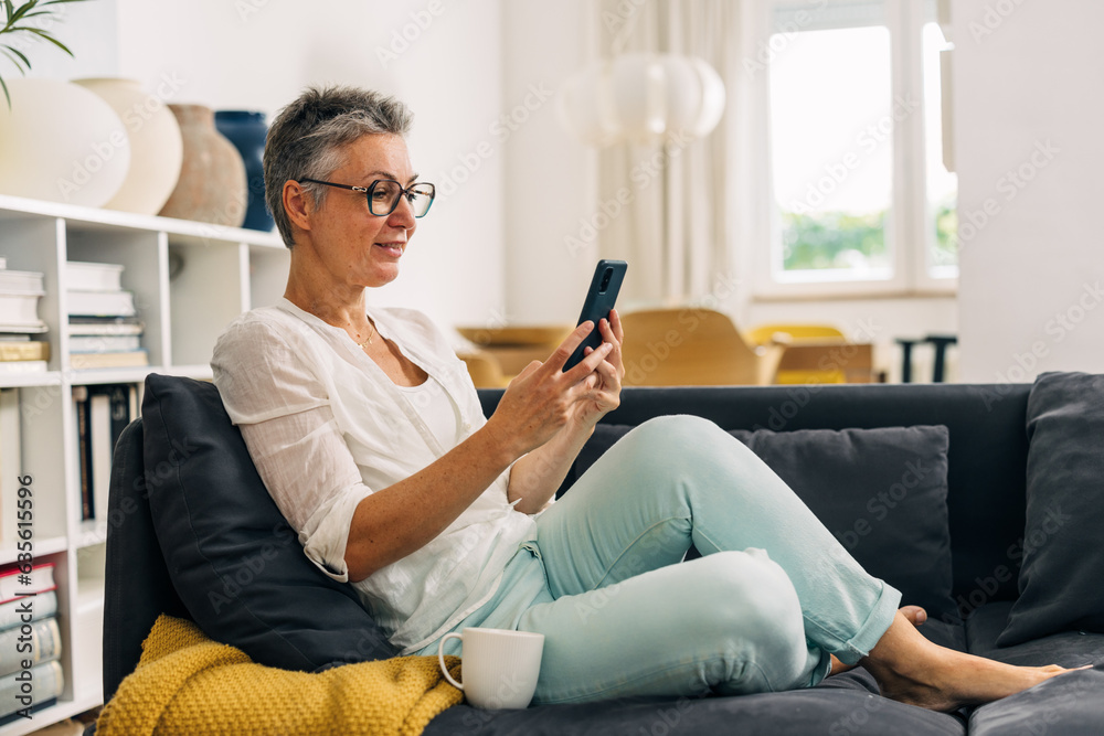 Obraz premium Beautiful mature woman with gray hair is using a mobile phone at home.