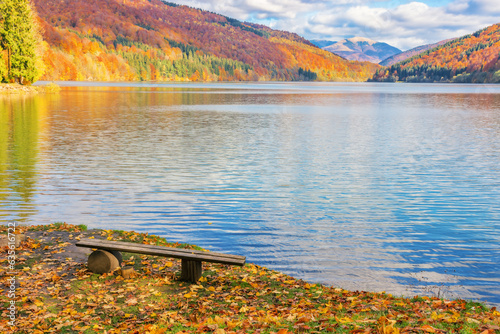 wooden bench on the shore of a tereblya water reserve. colorful scenery of carpathian mountains on a sunny day in autumn. travel and relaxation concept photo