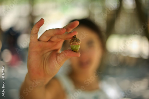 Pequenos gestos, grandes começos: Uma criança segura entre os dedos uma semente de carvalho, plantando as raízes da esperança e a promessa de um futuro florescente. photo