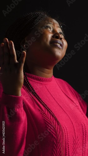 vertical video Graceful black woman gazing upwards with palms extended in gesture of reverance and adoration. Side-view portrait of african american lady engaged in prayerful reflection in isolated photo