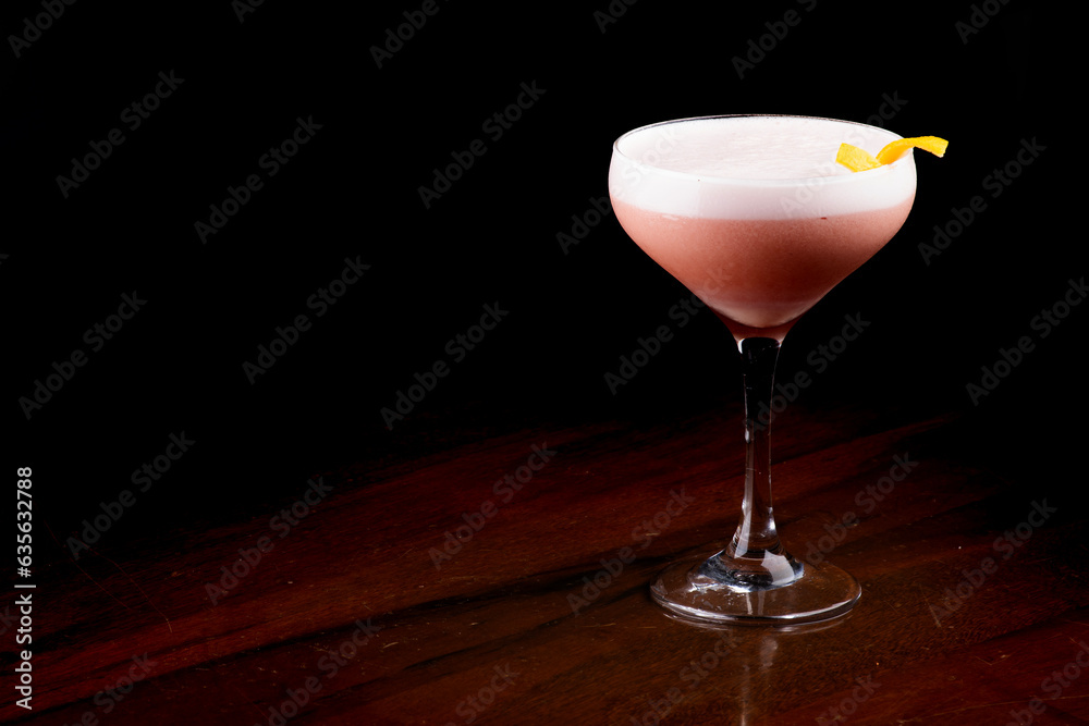 cocktail glass with creamy white foam and berries with orange peel topping isolated on black background at an angle cocktail glass with creamy white foam and berries with orange peel topping isolated on black background at an angle