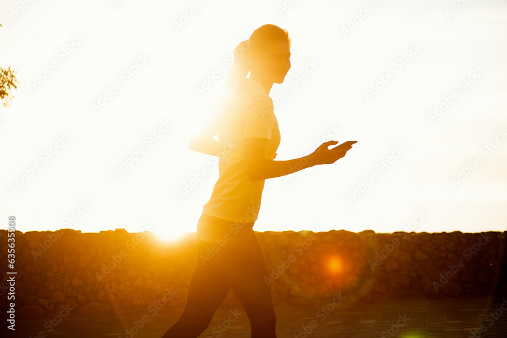 Close-up portrait of young woman in sportswear, jogging in the park by the sea, holding a smartphone