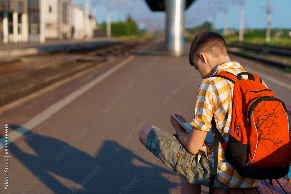 a student poses at a railway station, a boy is waiting for a train on the platform, reading books and doing homework, goes to study, the concept of education