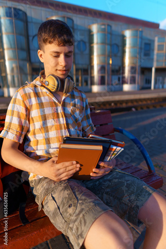 a student poses at a railway station, a boy is waiting for a train on the platform, reading books and doing homework, goes to study, the concept of education