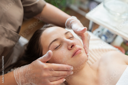 Cosmetologist washing and cleaning client face before procedure of ultrasound face cleaning. Preparations before ultrasonic face cleaning procedure on female face