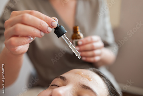 Microneedle mesotherapy in cosmetology clinic. Doctor drops some medicine to the forehead of a girl client before using meso roller with microneedles