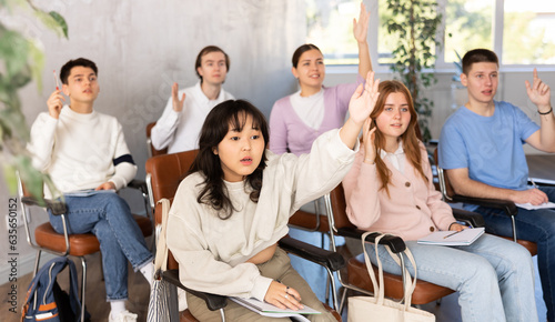 High school students sitting on chairs and raising hands to answer in lecture room
