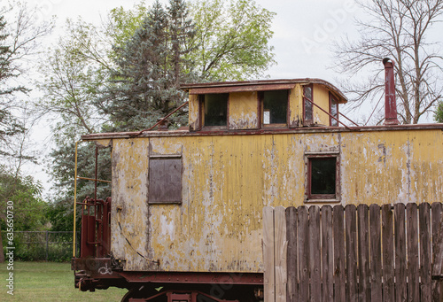 Exterior view of a deteriorating yellow 19th century railway train caboose car with weathered wood siding.