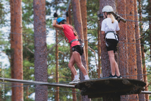 View of high ropes course, process of climbing in amusement acitivity rope park, passing obstacles and zip line on heights in climbing safety equipment gear between the trees om heights, summer day photo