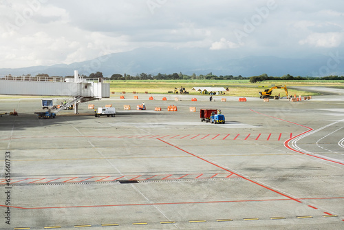Cali airport cargo terminal. Runway and passenger and baggage loading area of an airport. Several workers, baggage carts and a backhoe are on site performing maintenance.