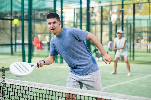 Caucasian teenage boy in sportswear playing padel tennis match during training on court. © JackF