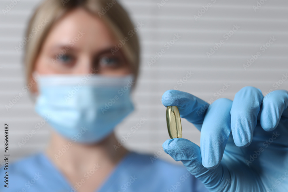 Doctor holding pill on light background, selective focus. Space for text