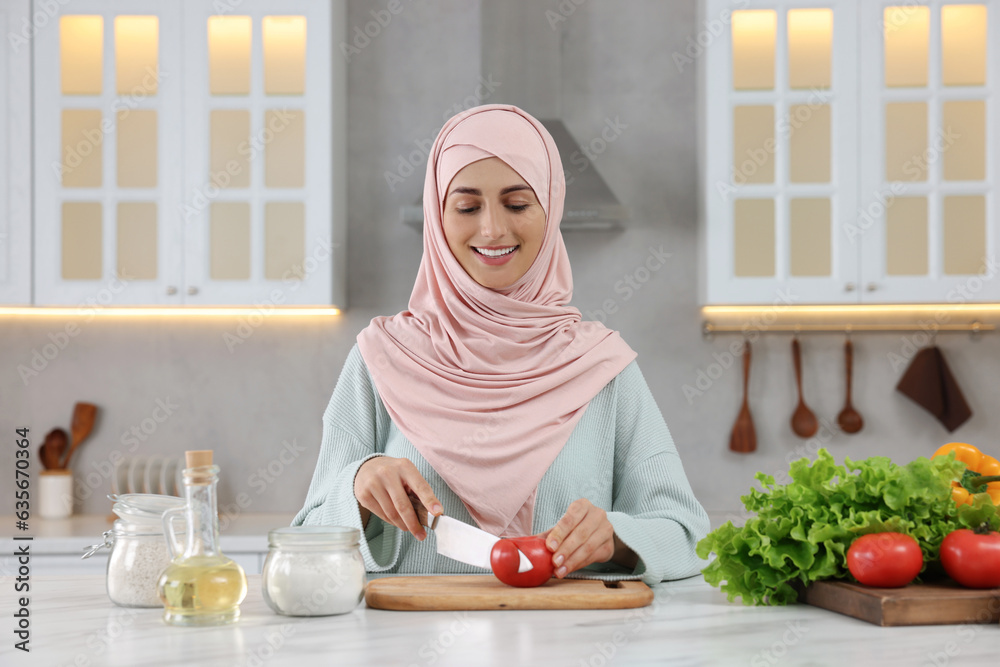 Muslim woman making delicious salad with vegetables at white table in kitchen Muslim woman making delicious salad with vegetables at white table in kitchen