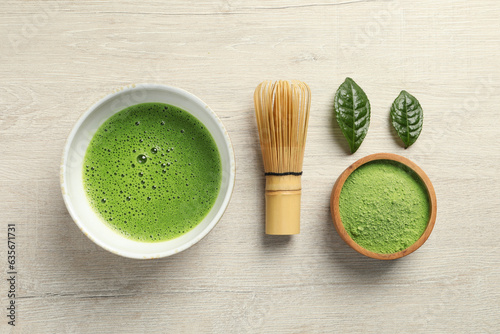 Cup of fresh matcha tea, green powder and bamboo whisk on white wooden table, flat lay