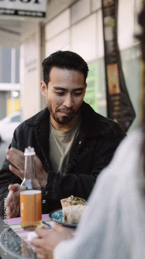 Happy young multiracial couple in casual clothing talking and eating during lunch at vegan cafe Happy young multiracial couple in casual clothing talking and eating during lunch at vegan cafe