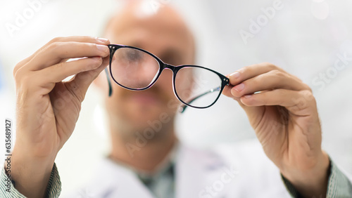 Male optician and optometrist, background of shop window with different models of glasses holding glasses in hand checking glasses eye care concept