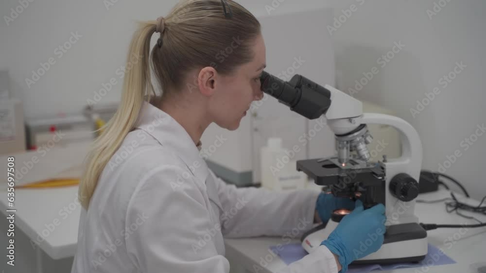 Female scientist using microscope while working in laboratory. Lab for modern medical research. Woman laboratory assistant looking in microscope analyzing samples biochemical substances, blood tests. Female scientist using microscope while working in laboratory. Lab for modern medical research. Woman laboratory assistant looking in microscope analyzing samples biochemical substances, blood tests.
