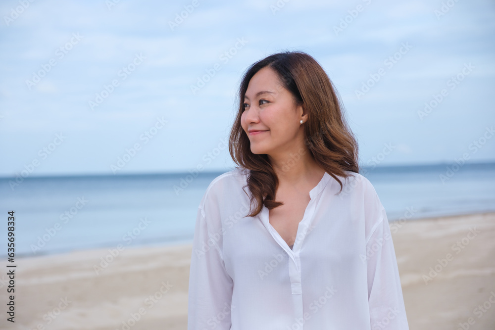 Portrait image of a beautiful young asian woman while strolling on the beach with the sea and blue sky Portrait image of a beautiful young asian woman while strolling on the beach with the sea and blue sky