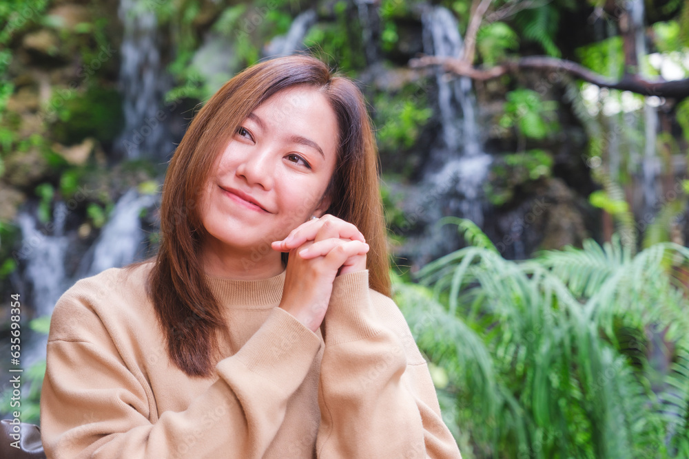 Portrait image of a young woman holding hands and relaxing in the garden with waterfall Portrait image of a young woman holding hands and relaxing in the garden with waterfall