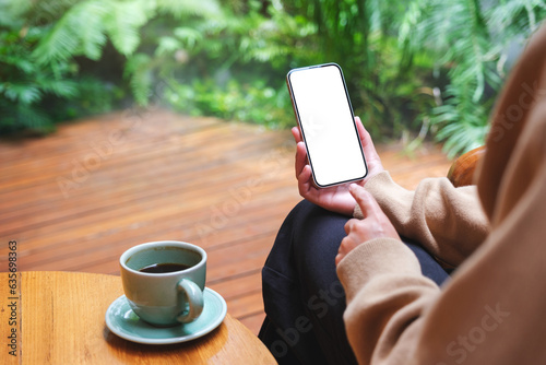 Mockup image of a woman holding mobile phone with blank white desktop screen in the garden